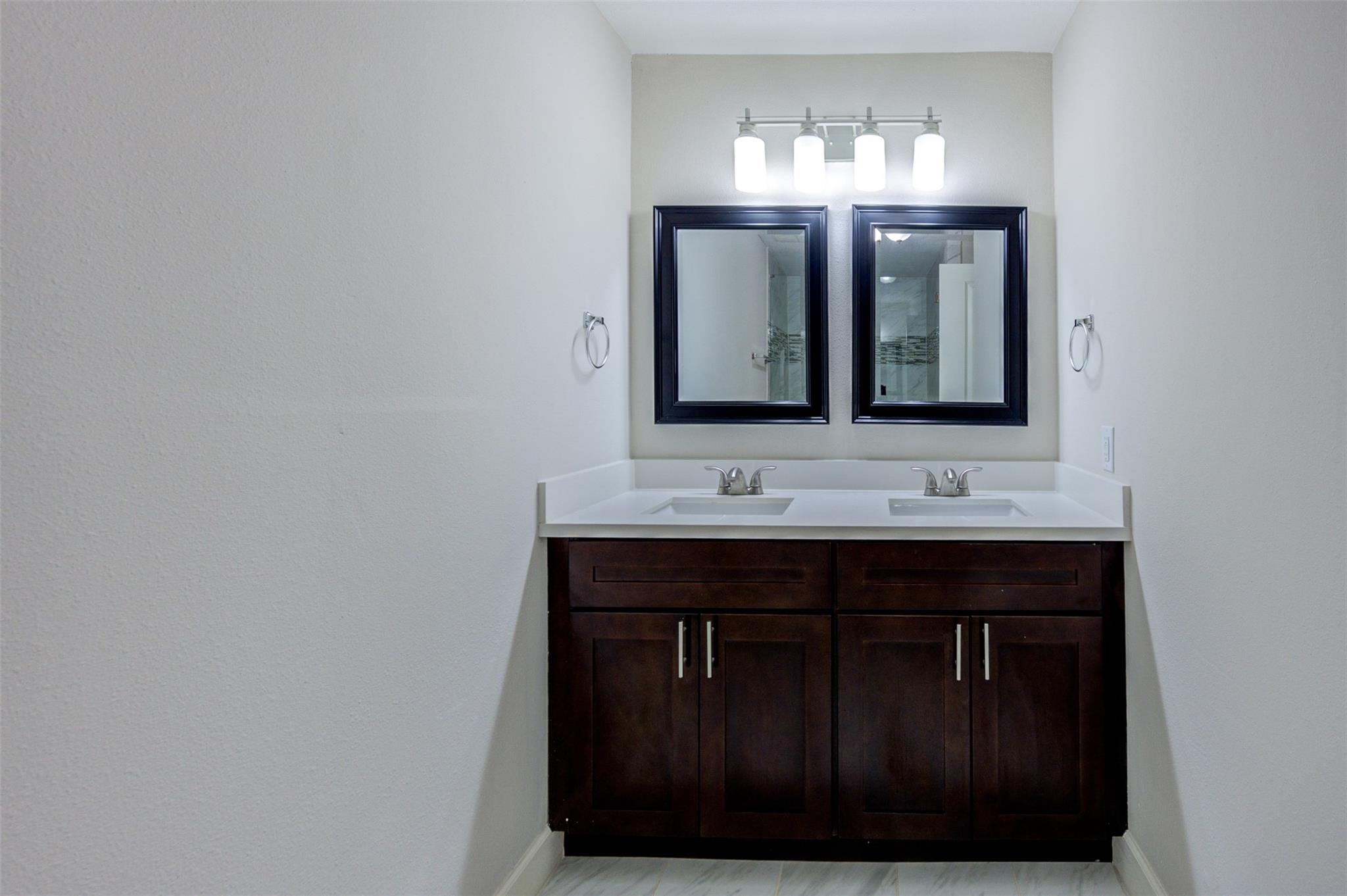 Bathroom with a double-sink white vanity, dark wood cabinets, and two framed mirrors.