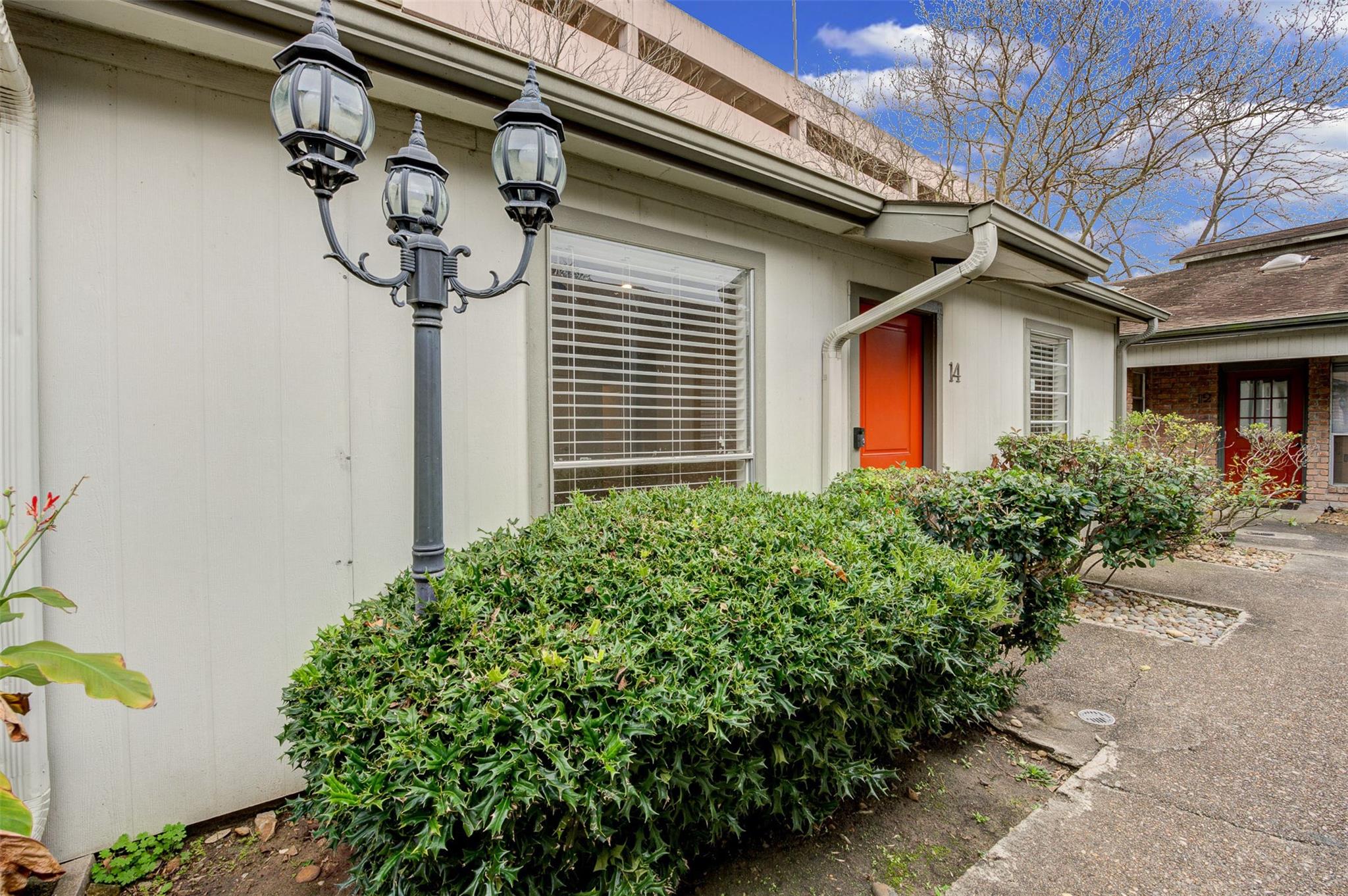 Townhome entrance with a red-orange door marked 14, white siding, trimmed hedges, and a three-lantern post.