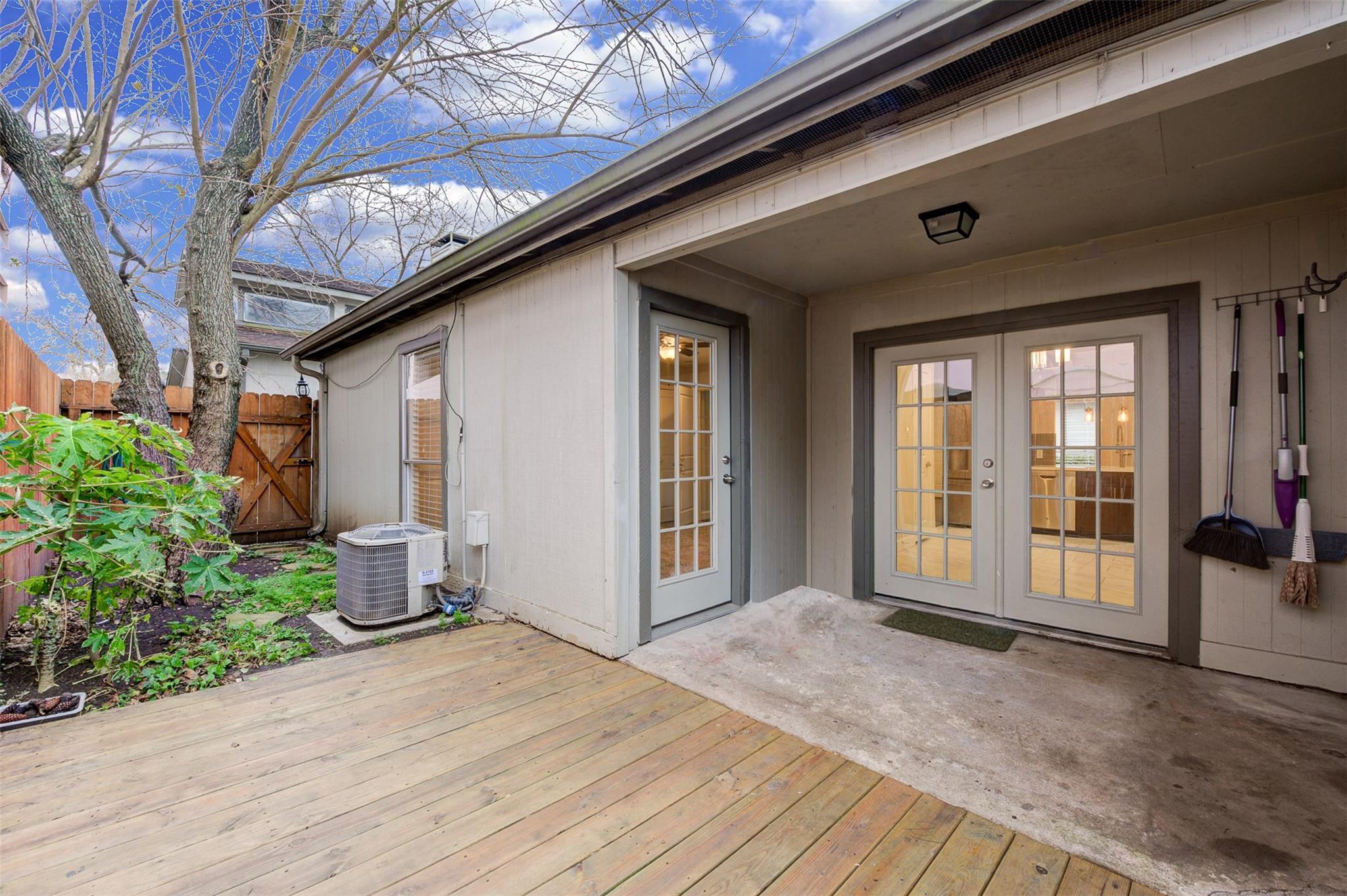 Covered backyard patio with French doors, wooden deck, and fenced garden.