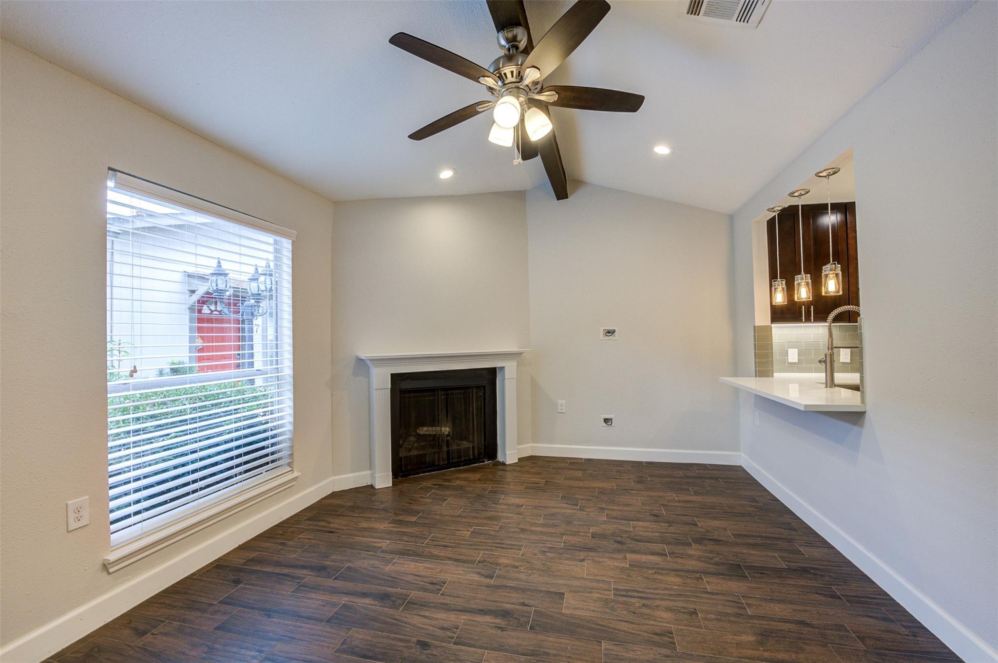Empty living room with dark tile floors, a fireplace, ceiling fan, and kitchen pass-through.
