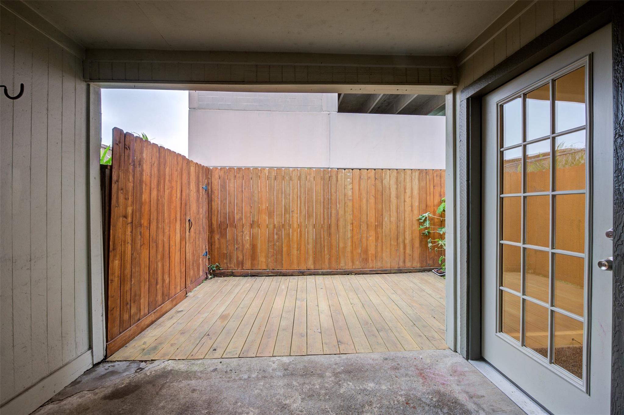 Covered private patio with a wood-plank deck, tall privacy fence, and divided-light French doors.