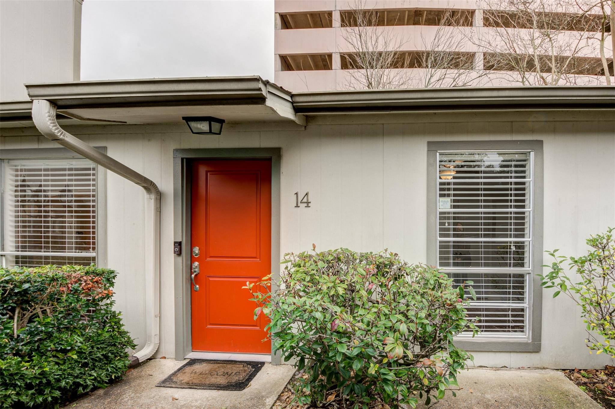 Residence entrance with a bright red door, number 14, barred windows, and shrubs.