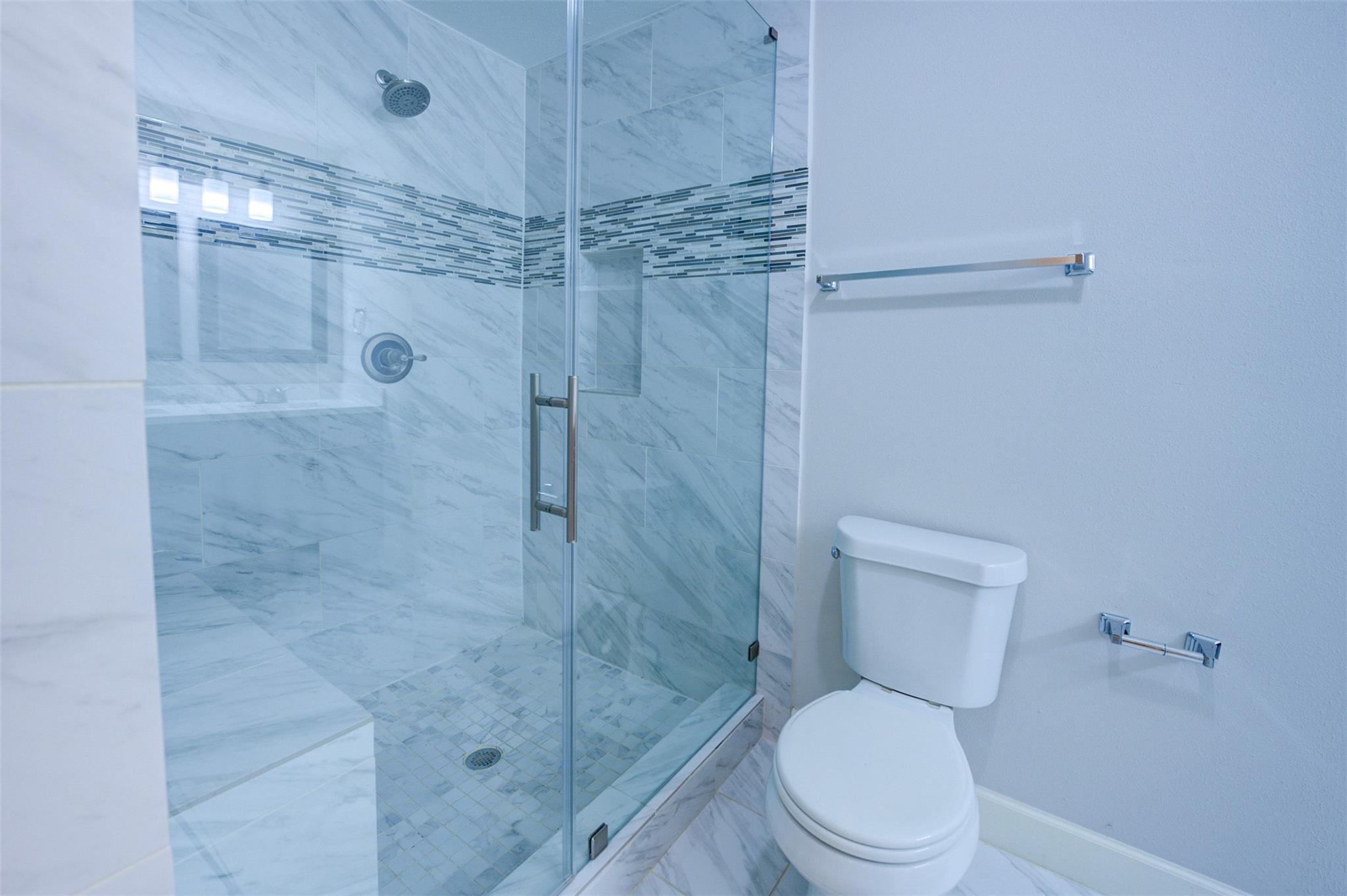 Bathroom with a glass walk-in shower, marble-look tile, mosaic accent band, and white toilet.