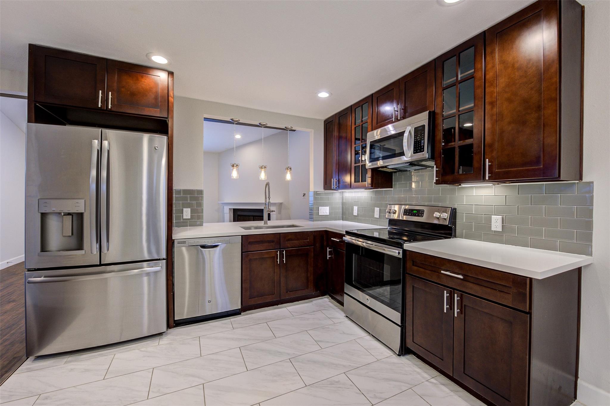 Kitchen with dark wood cabinets, stainless steel appliances, gray tile backsplash, and white countertops.