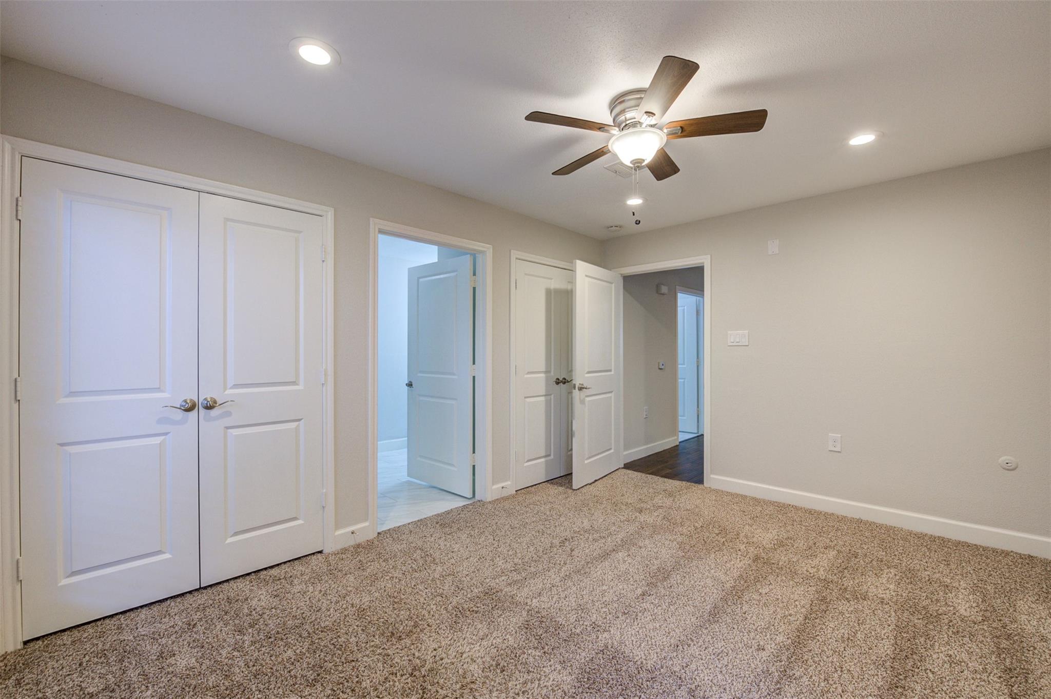 Vacant bedroom with beige carpet, white closet doors, and a ceiling fan with light.