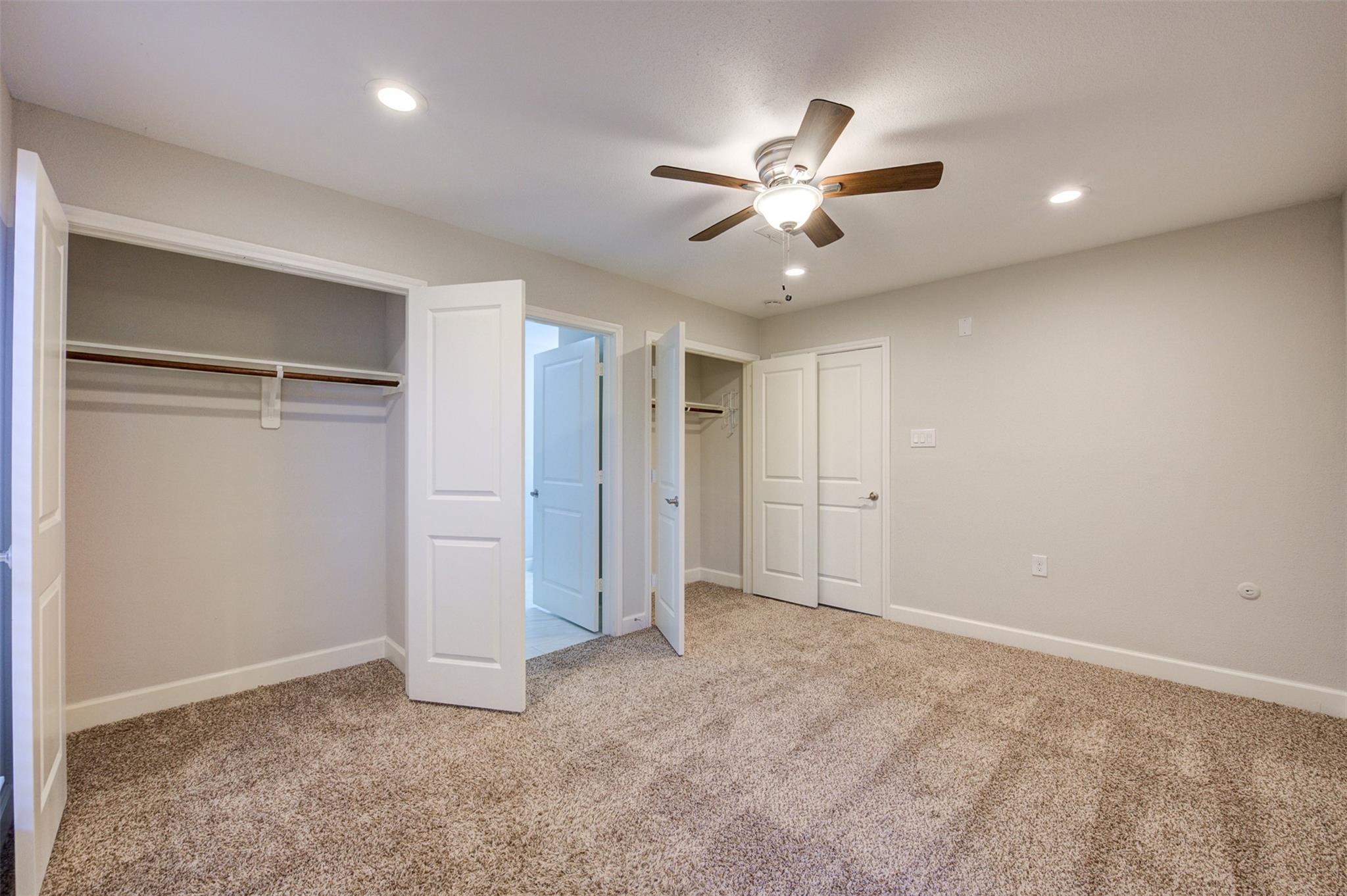 Vacant bedroom with beige carpet, two open closets, and a ceiling fan.
