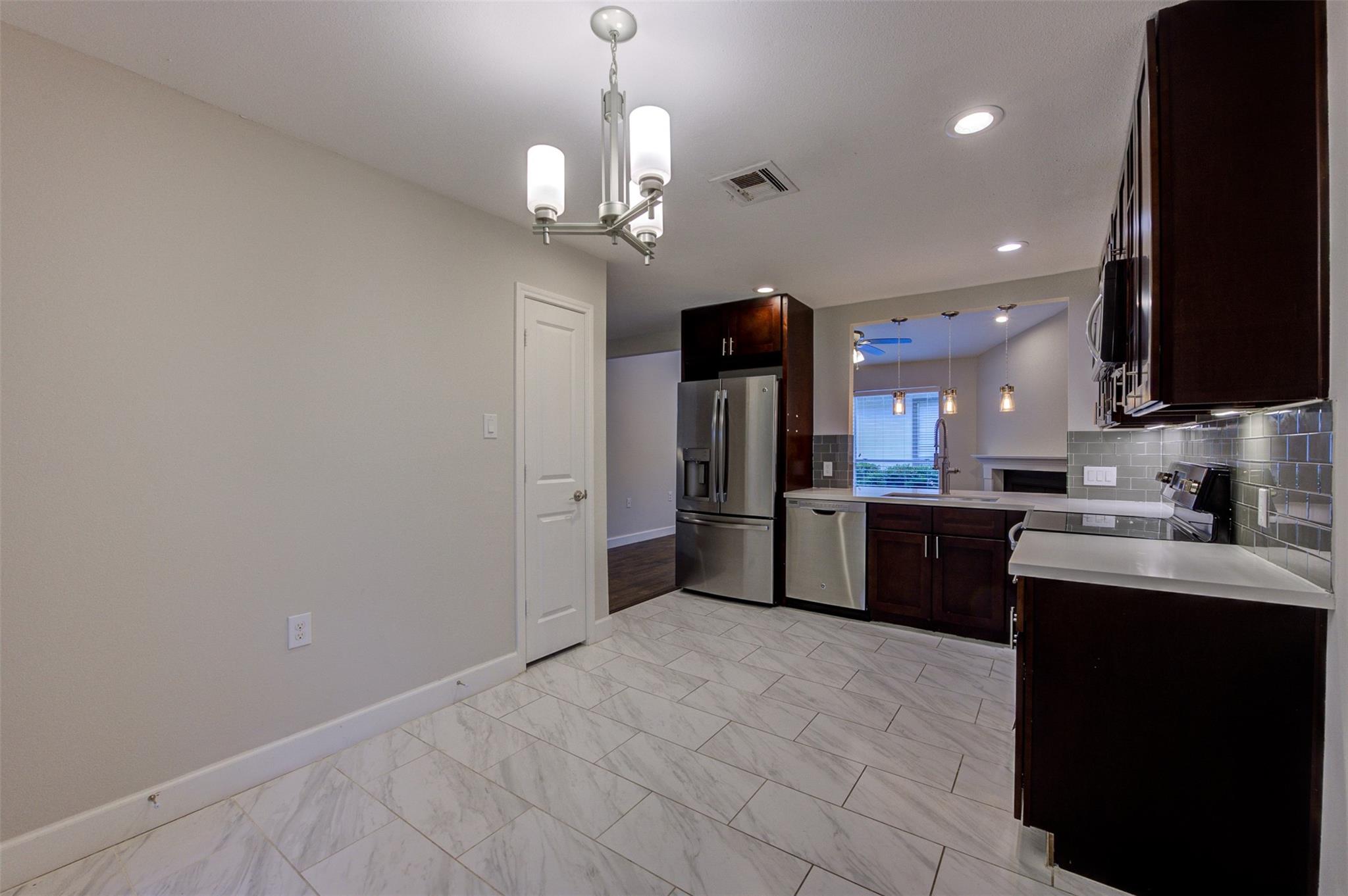 Kitchen with dark wood cabinets, stainless steel appliances, and white marble-look tile flooring.