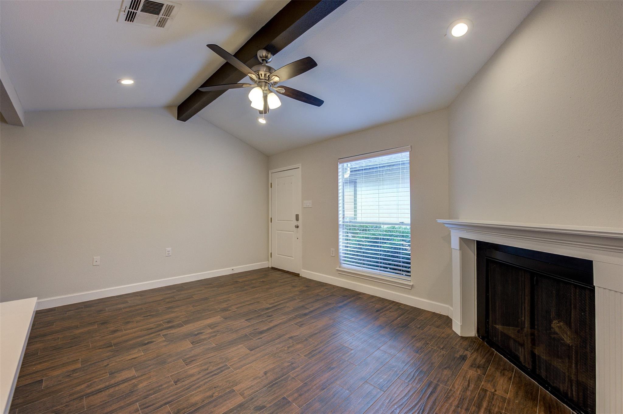 Vacant living room with a vaulted ceiling, dark tile floors, ceiling fan, and fireplace.