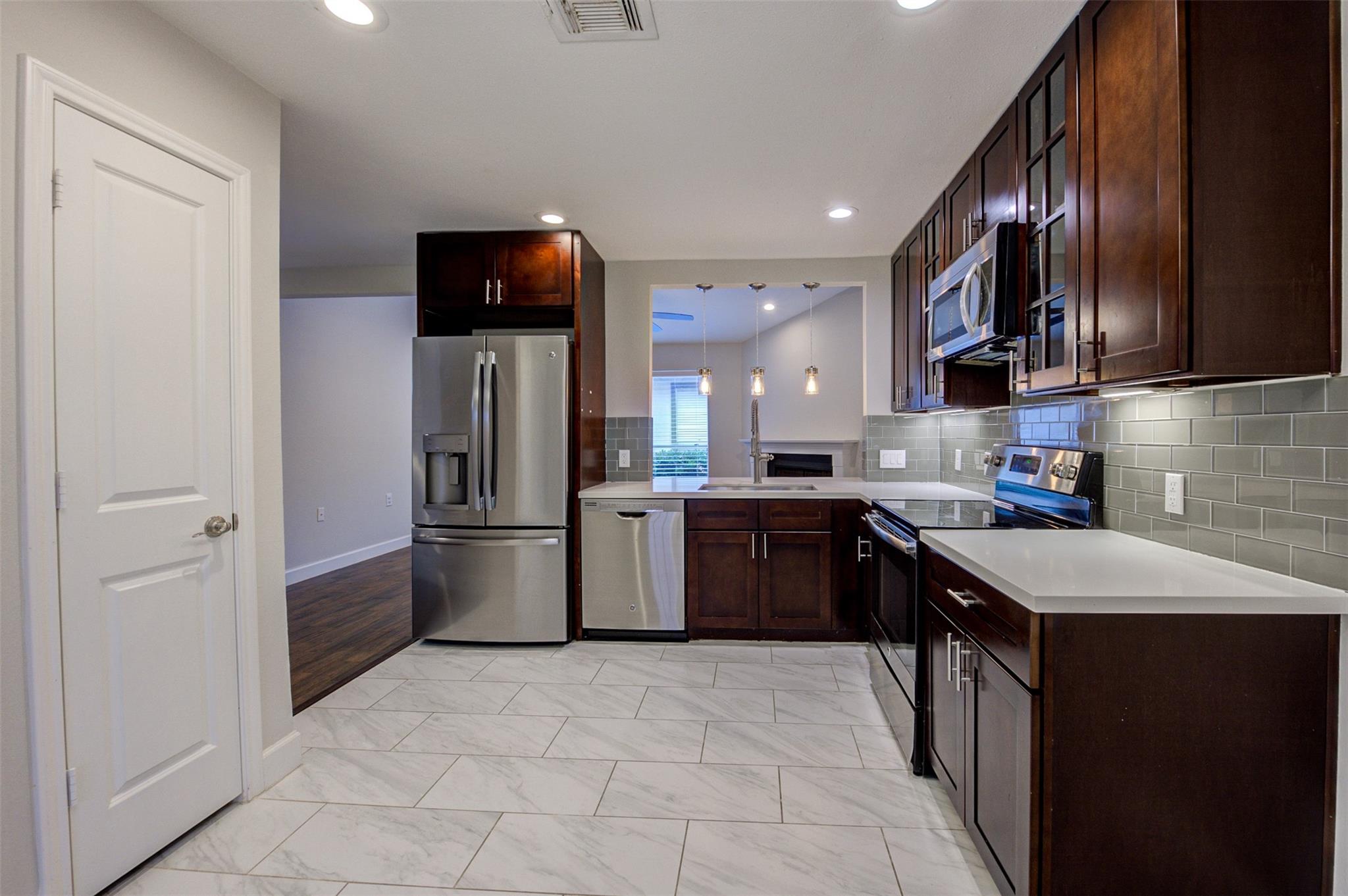 Kitchen with dark wood cabinets, stainless steel appliances, and light marble-look tile flooring.