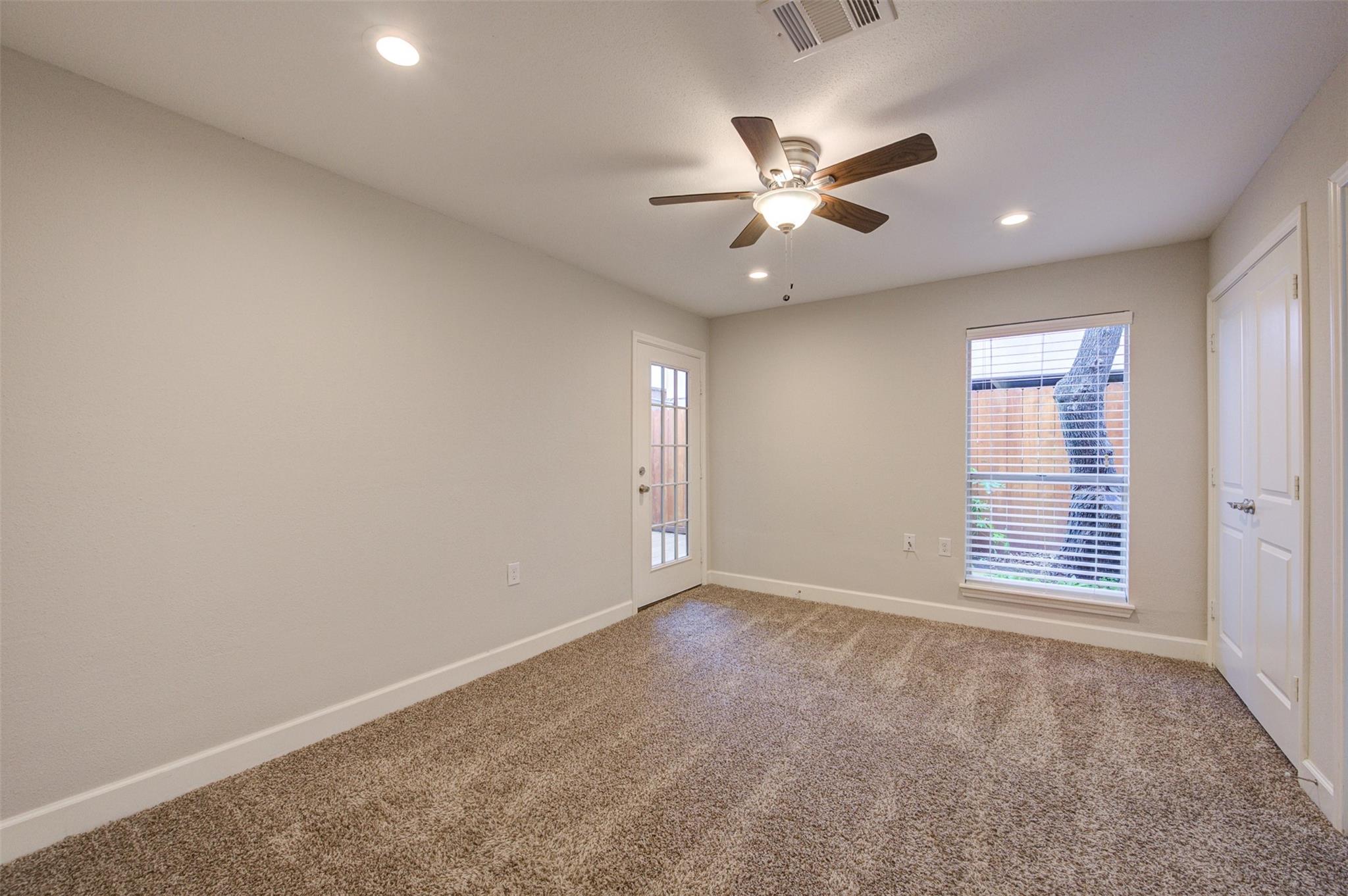 Empty carpeted bedroom with a ceiling fan, glass-paneled door, and window with blinds.