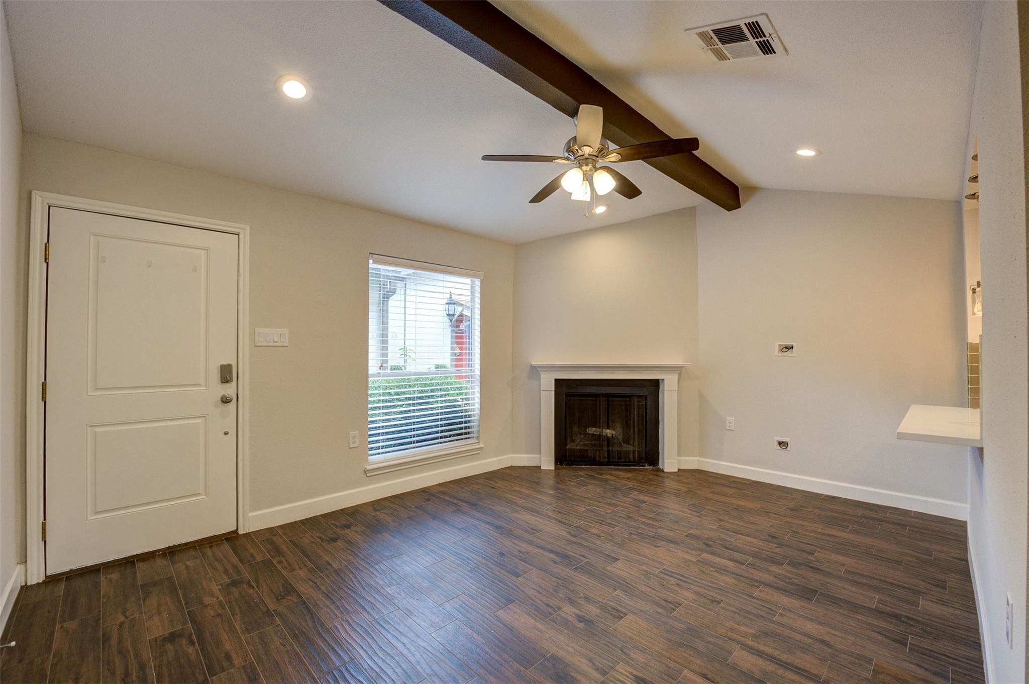 Vacant living room with vaulted ceiling, dark wood-look flooring, and corner fireplace.