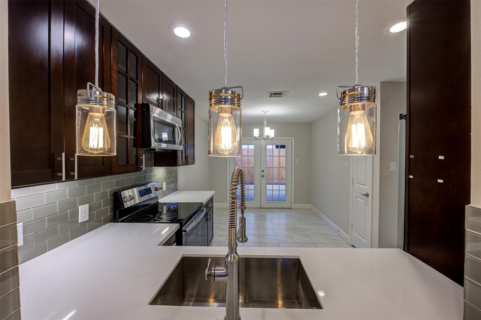 Modern kitchen with dark wood cabinets, gray tile backsplash, and three glass pendant lights over a sink.