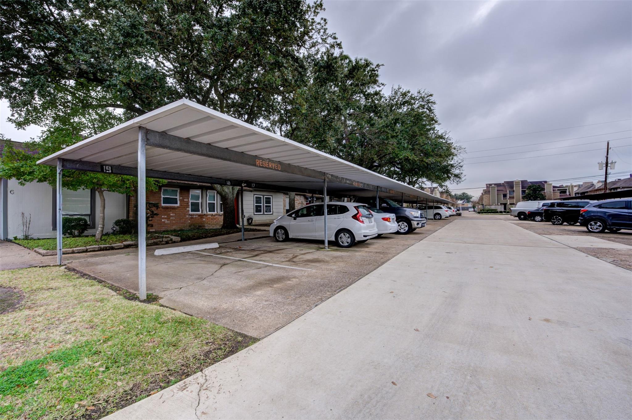 Residential property with covered parking, reserved spaces, and cars beside a brick facade.