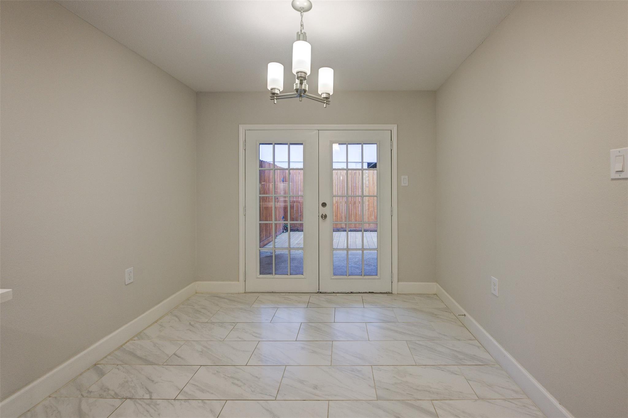 Empty dining area with marble-look tile, a chandelier, and glass double doors to a fenced patio.