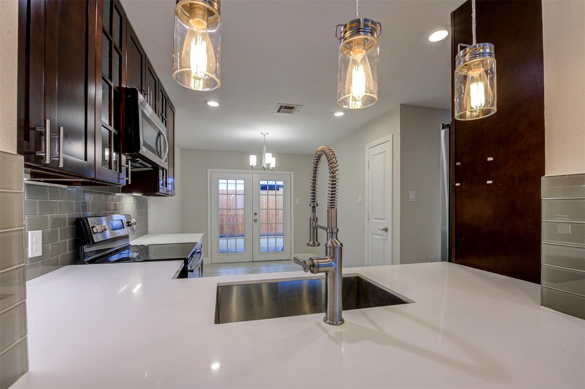 Modern kitchen with dark cabinets, white quartz counters, and a large island sink with spring-coil faucet.