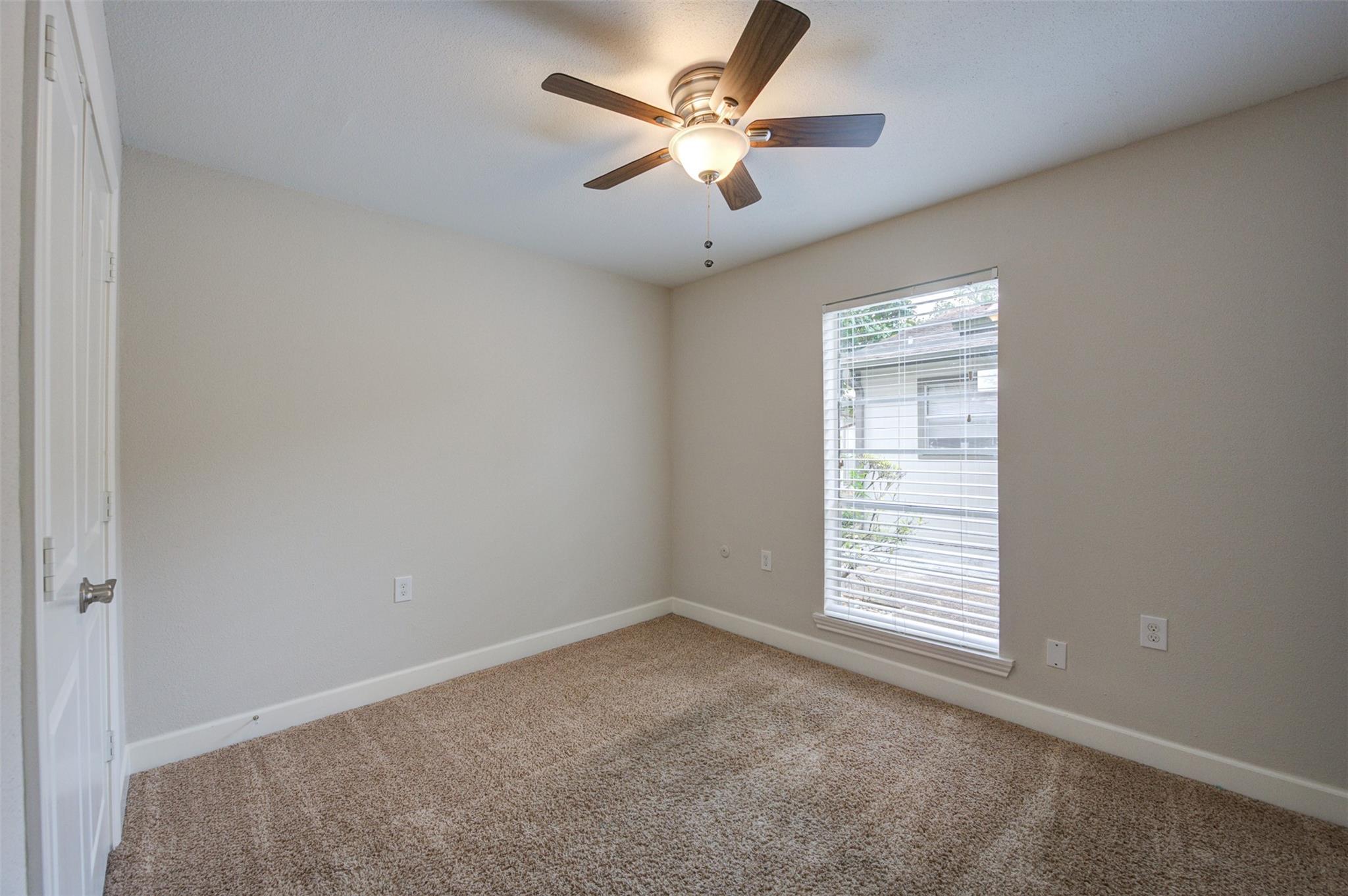 Unfurnished bedroom with beige carpet, a ceiling fan, and a window with white blinds.