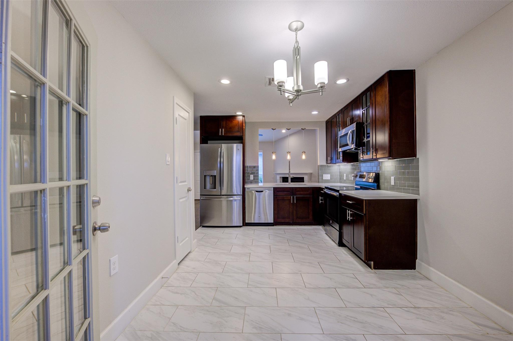 Kitchen with dark wood cabinets, stainless steel appliances, and large light tile flooring.