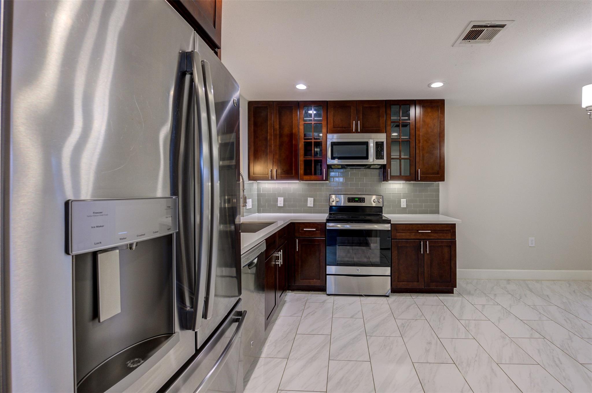 Kitchen with dark wood cabinets, stainless steel appliances, and marble-look tile flooring.