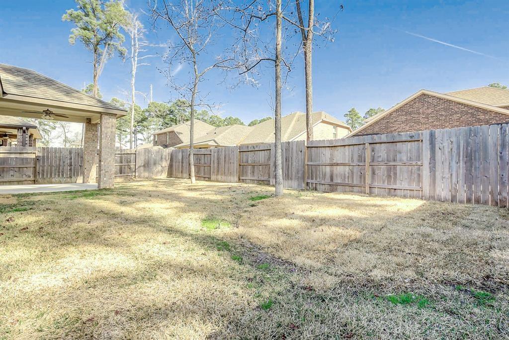 Fenced backyard with a broad lawn, leafless trees, and a covered patio.