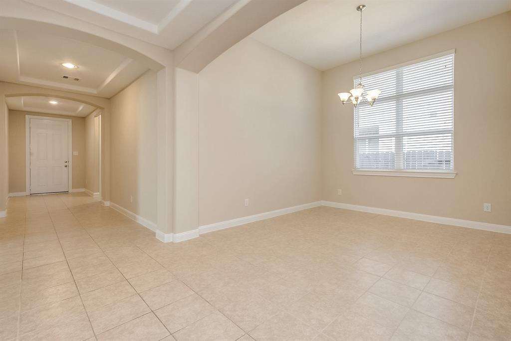 Empty tiled room with a chandelier, large window, and entry hall.