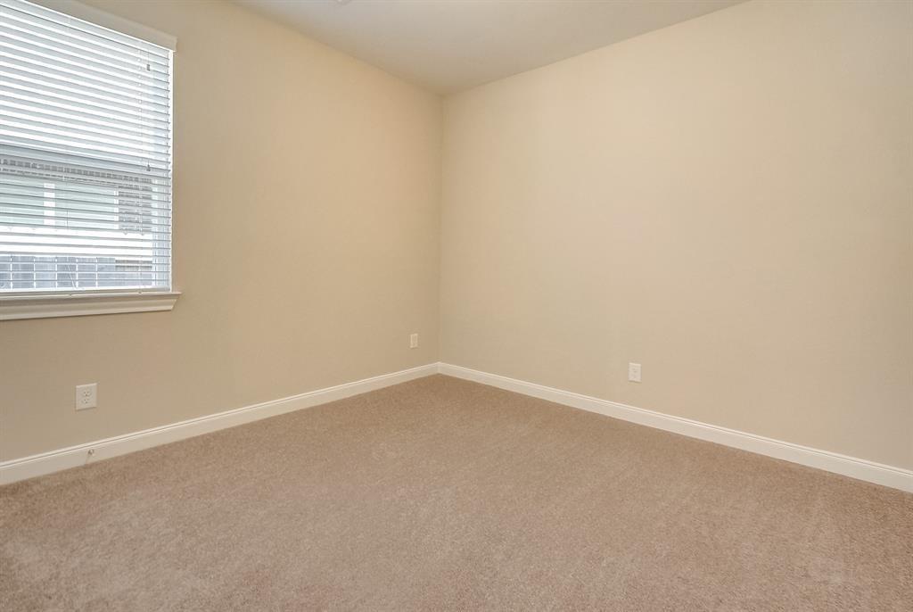 Empty carpeted room with beige walls and a window with horizontal blinds.