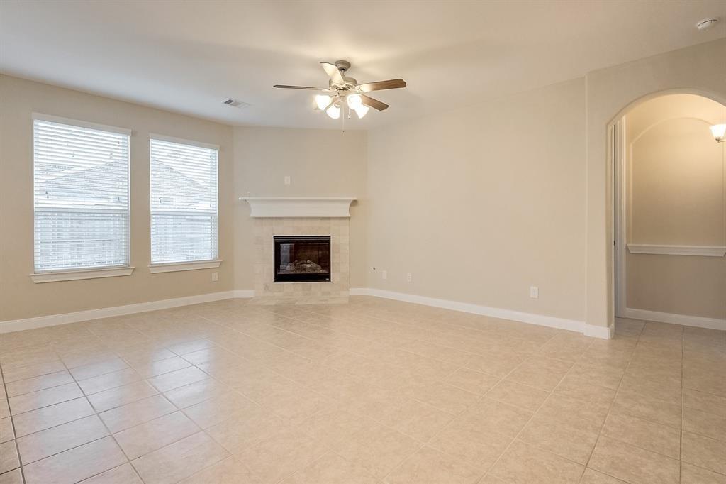 Empty living room with tiled floors, a fireplace, two windows, and a ceiling fan.
