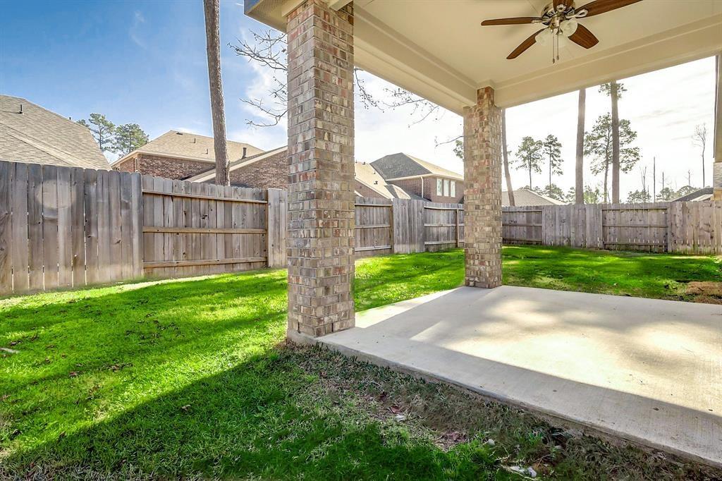 Covered patio with brick columns and ceiling fan overlooking a fenced backyard lawn.