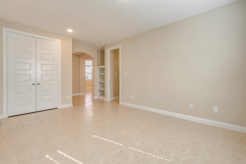 Empty bedroom with beige tile, double closet doors, and an arched window nook.