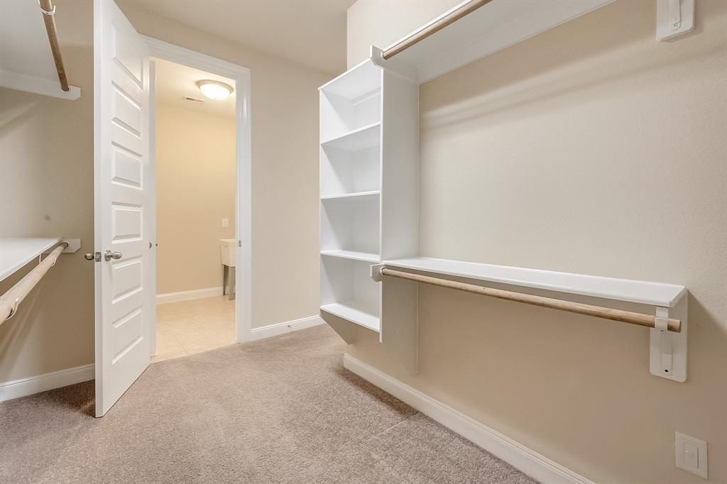 Walk-in closet with white built-in shelves, hanging rods, and an open door to a tiled room.