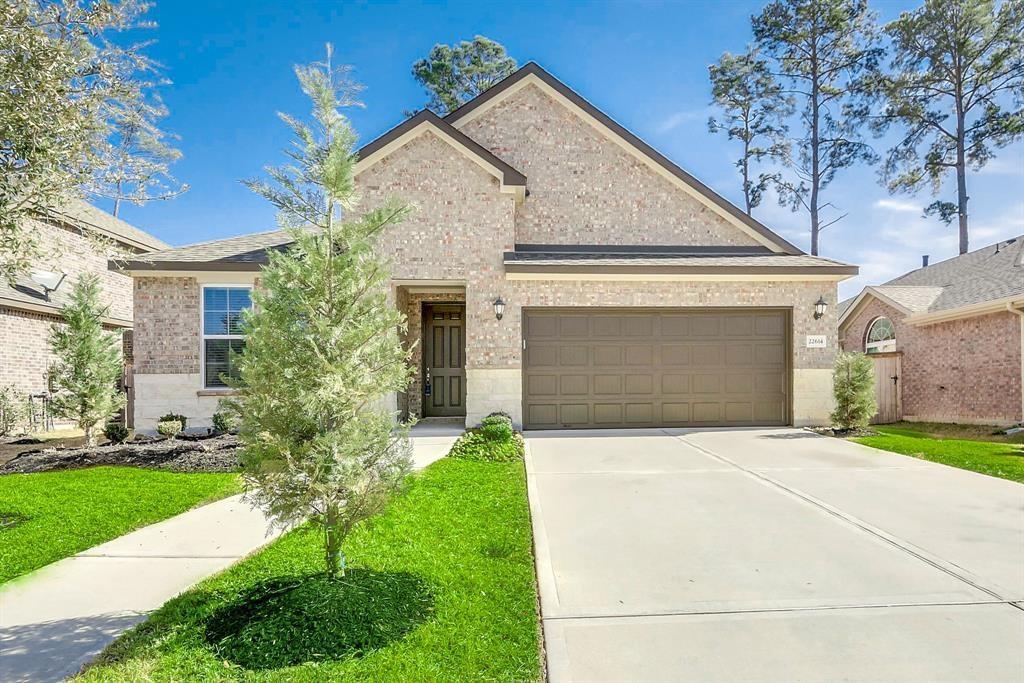 Brick home with a two-car garage, broad driveway, green lawn, and young trees.