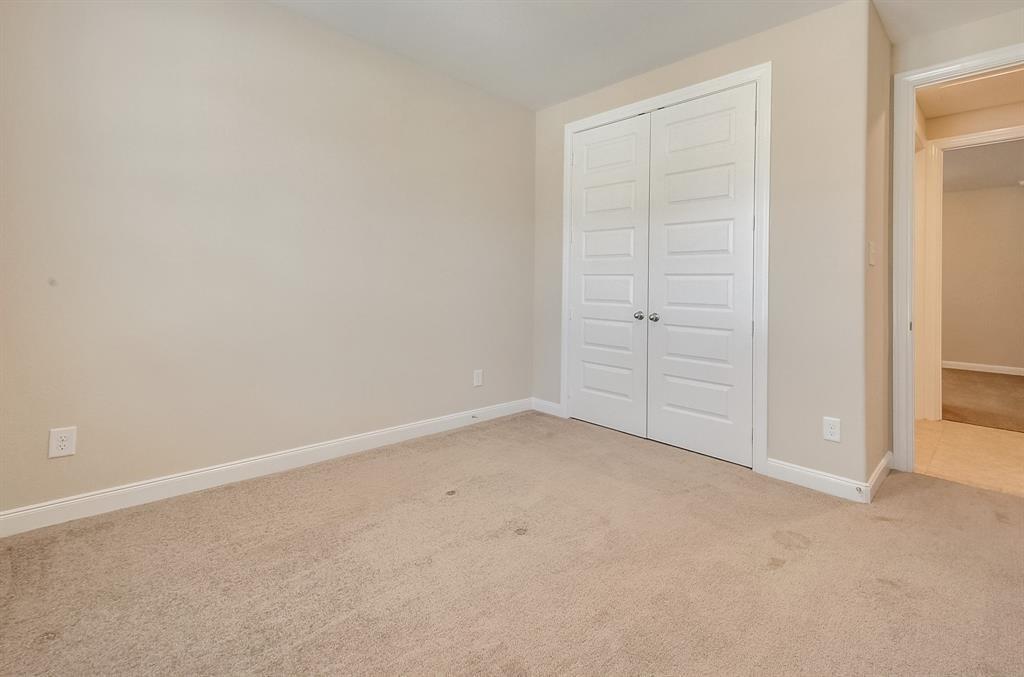 Empty carpeted bedroom with white double closet doors and an adjoining doorway.