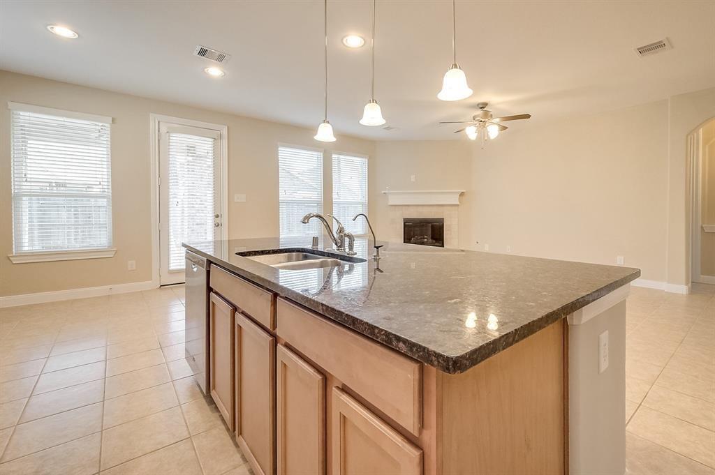 Unfurnished kitchen with a large dark-stone island, double-basin sink, and fireplace beyond.