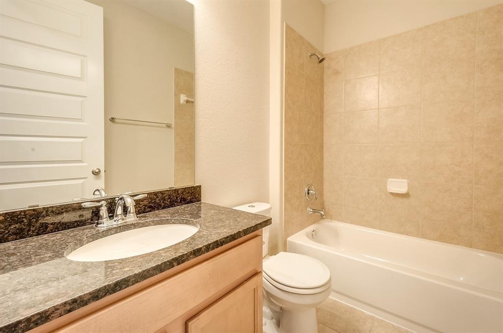 Bathroom with a granite vanity, white toilet, and bathtub with beige tile surround.