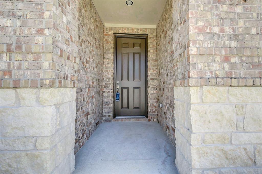 Recessed front entrance with a dark paneled door, brick walls, and pale stone columns.