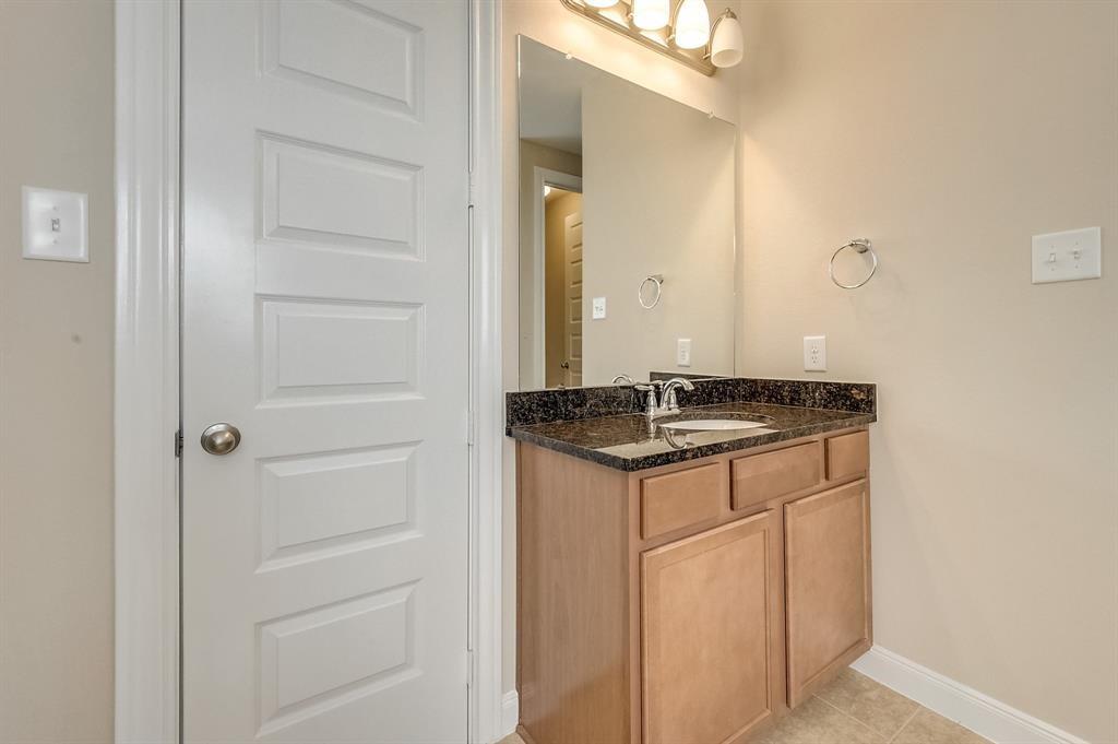 Bathroom vanity with a single sink, dark granite countertop, and light wood cabinets.