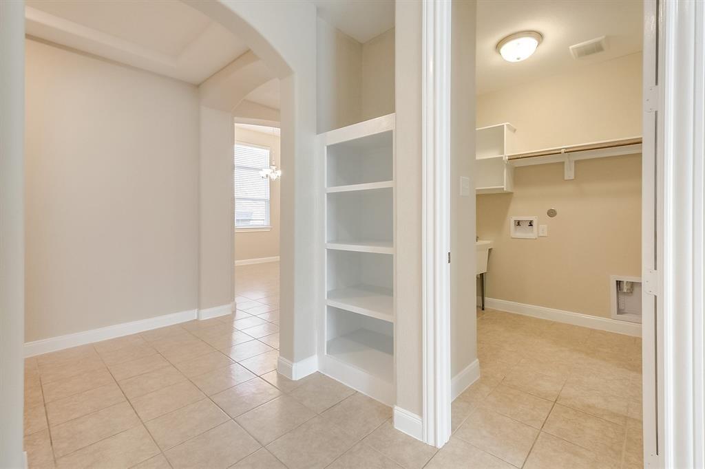 Vacant laundry room with beige tile floors, a utility sink, hookups, and built-in shelving.