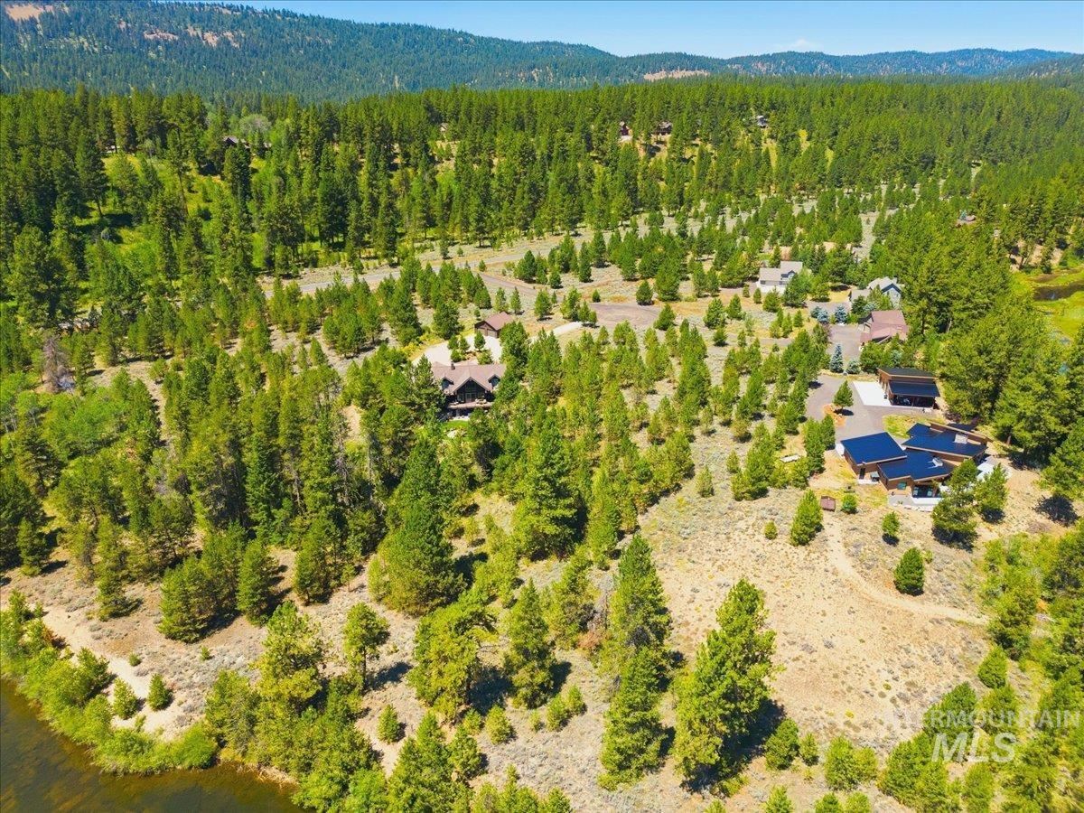 Aerial view of a wooded mountain neighborhood with homes, open lots, and distant ridgelines.