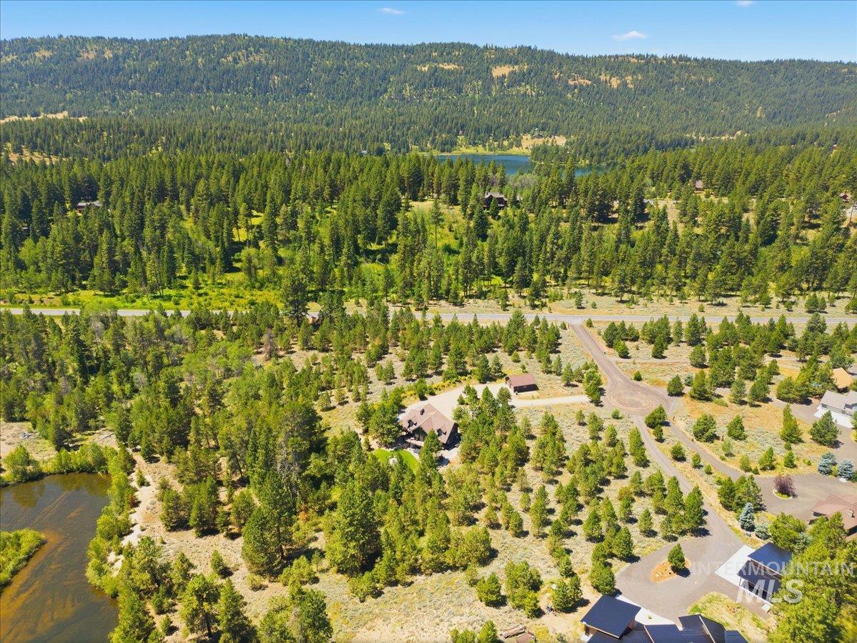Aerial view of a wooded McCall property with homes, a road, pond, and mountain backdrop.