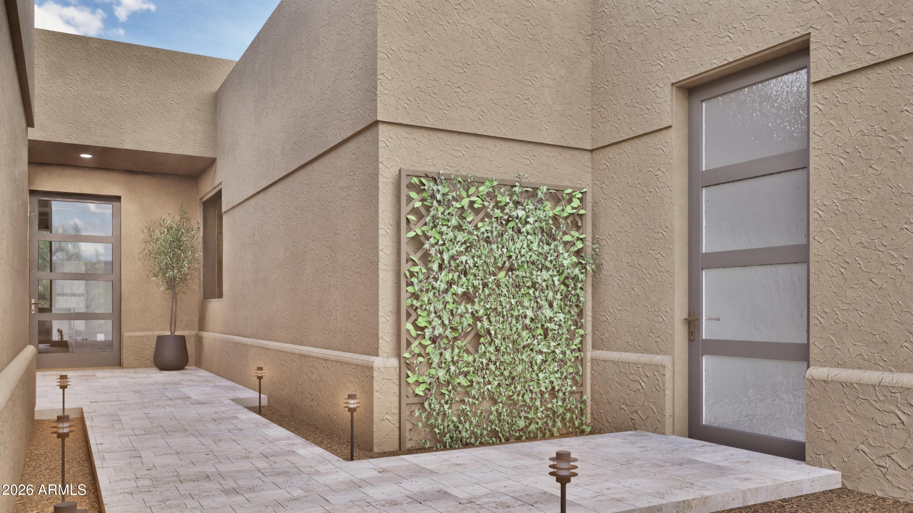Stucco home entry courtyard with a leafy trellis, stone paving, and modern glass-paneled doors.