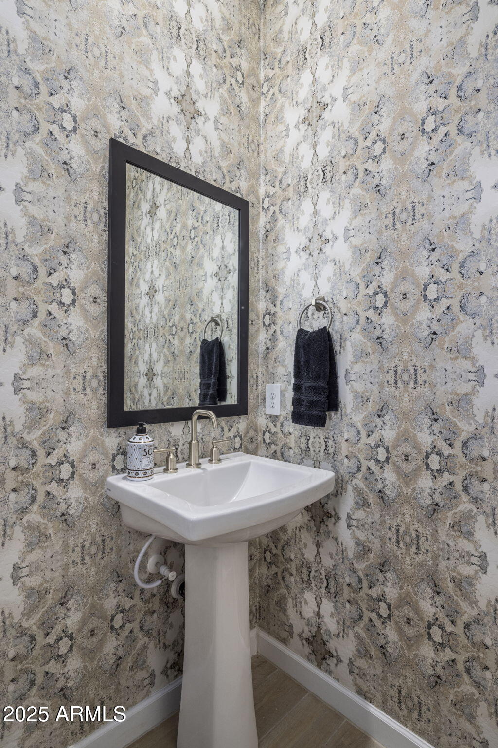 Powder room pedestal sink beneath a black-framed mirror, surrounded by bold patterned wallpaper.