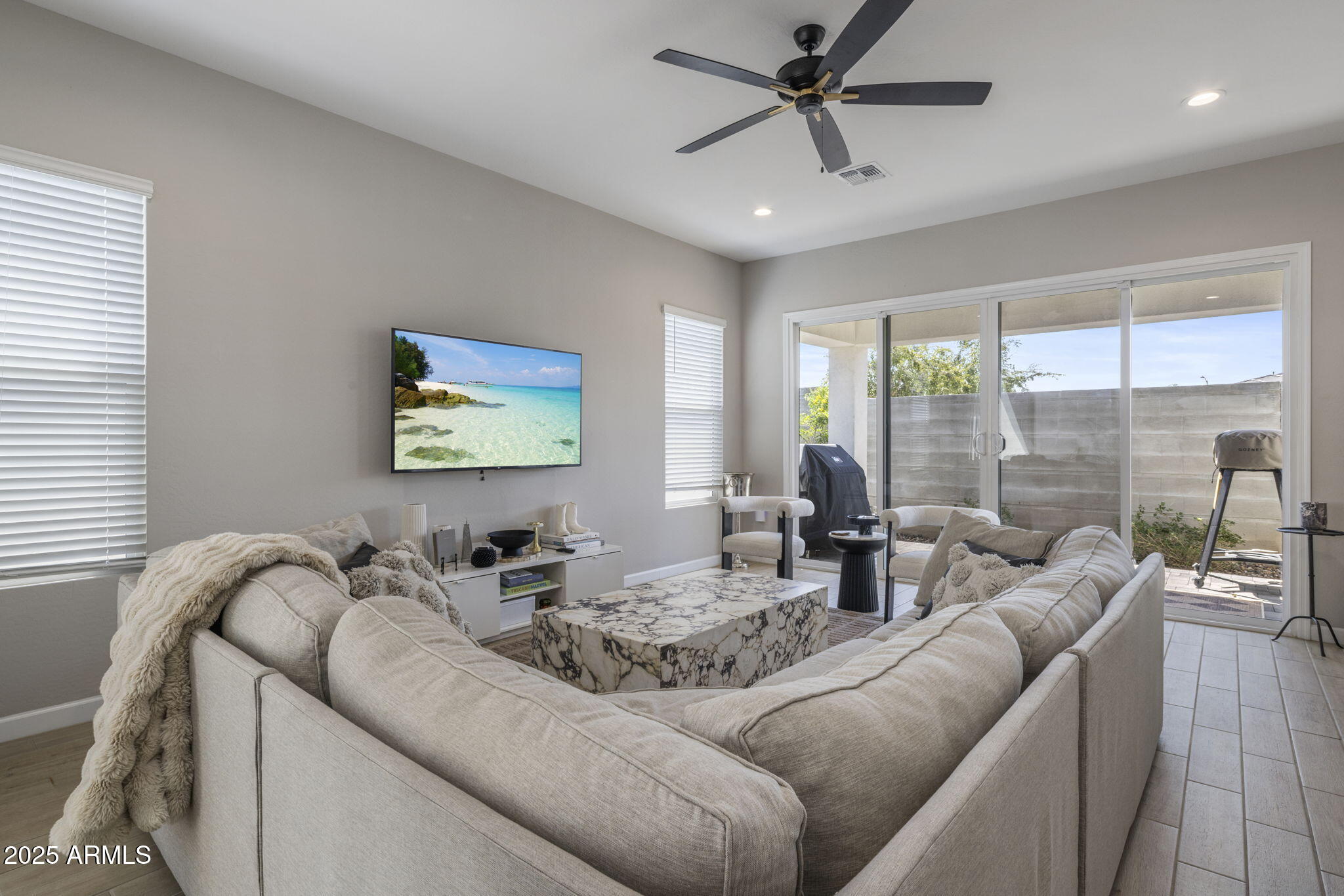 Staged living room with a cream sectional, marble-patterned coffee table, and sliding glass doors to a patio.