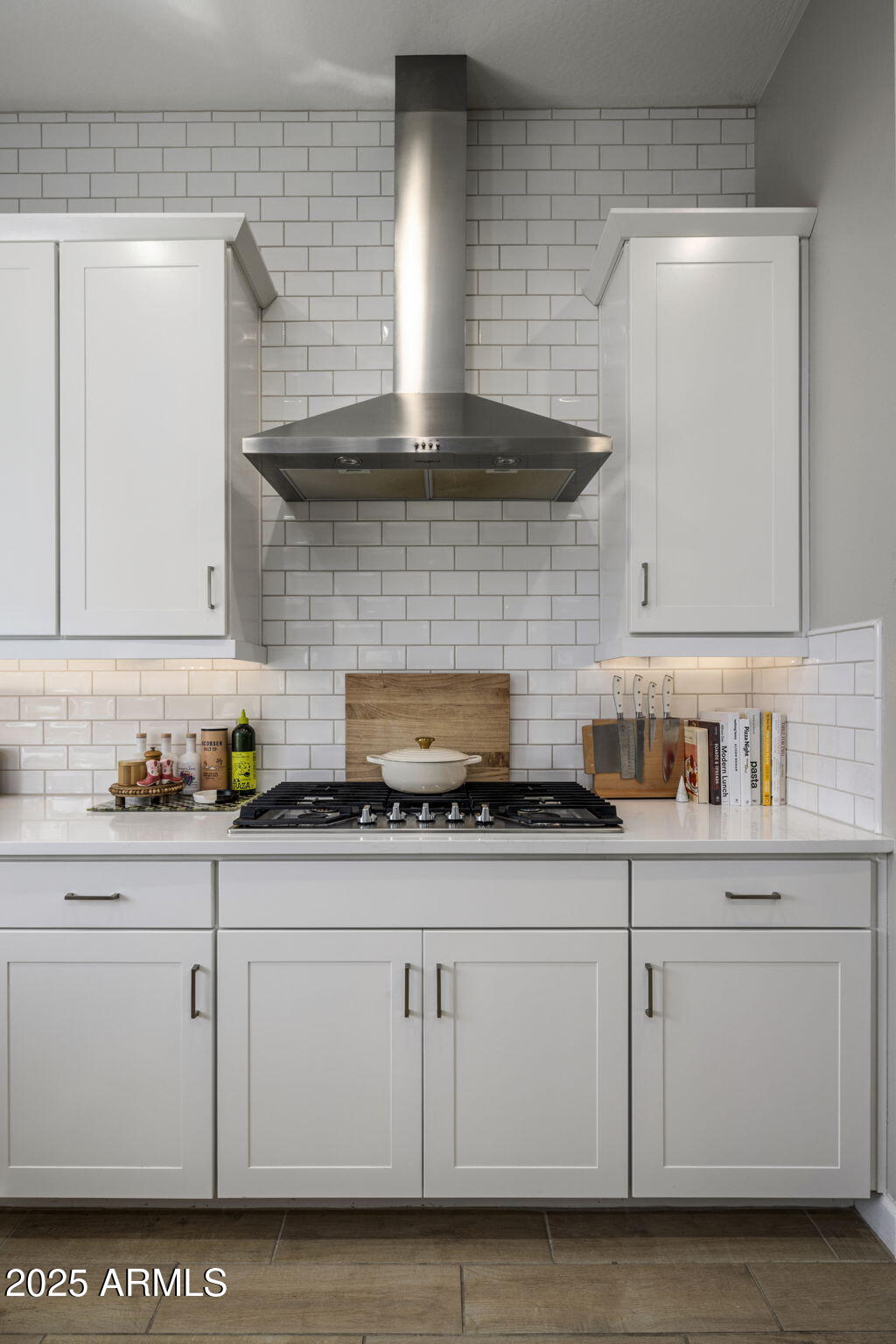 Kitchen with white shaker cabinets, subway tile backsplash, and a stainless steel range hood over a gas cooktop.