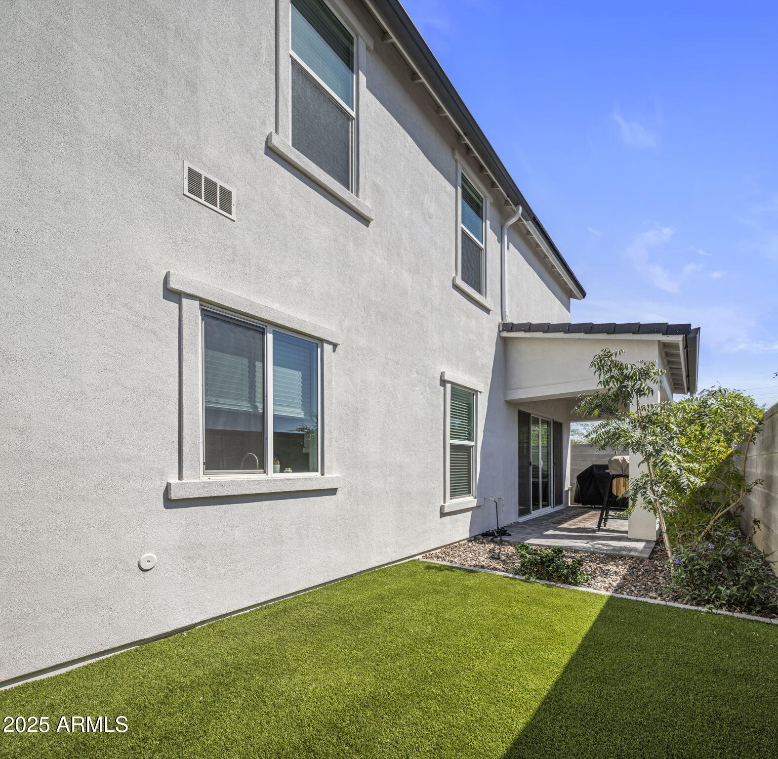 Two-story stucco home beside a green lawn, with a covered patio and sliding glass doors.