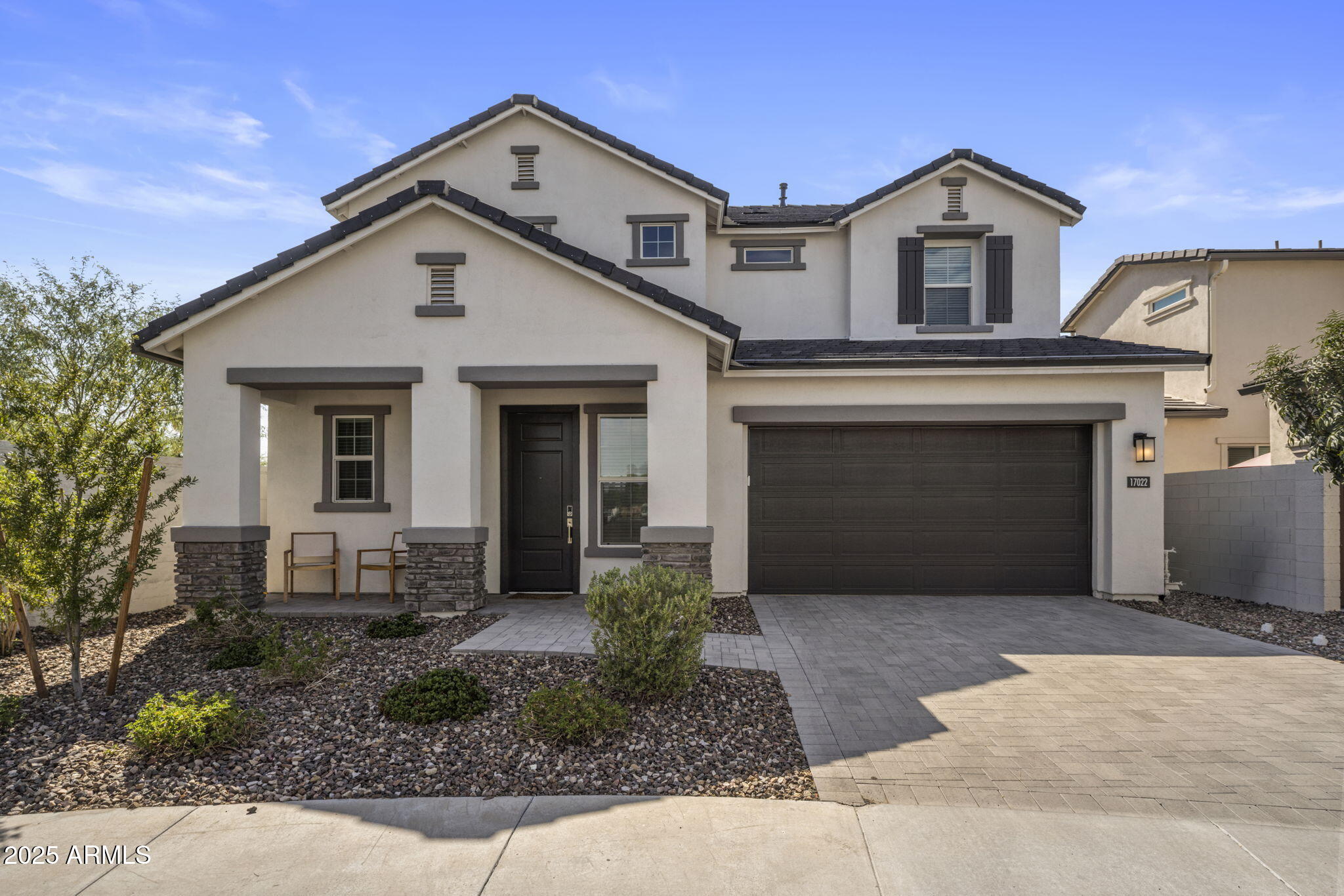 Two-story beige stucco home with dark trim, a covered porch, and a two-car garage.