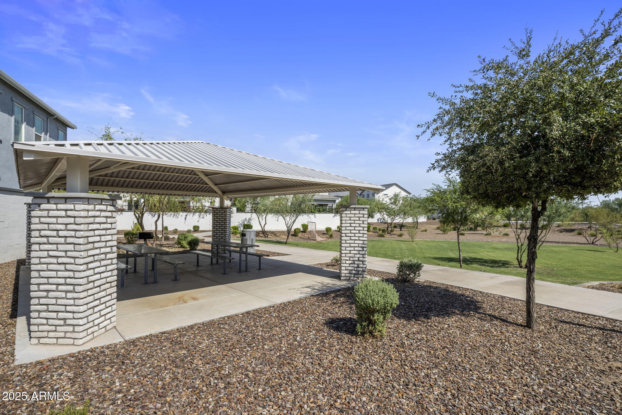 Covered picnic pavilion with white brick columns and picnic tables beside a landscaped lawn.
