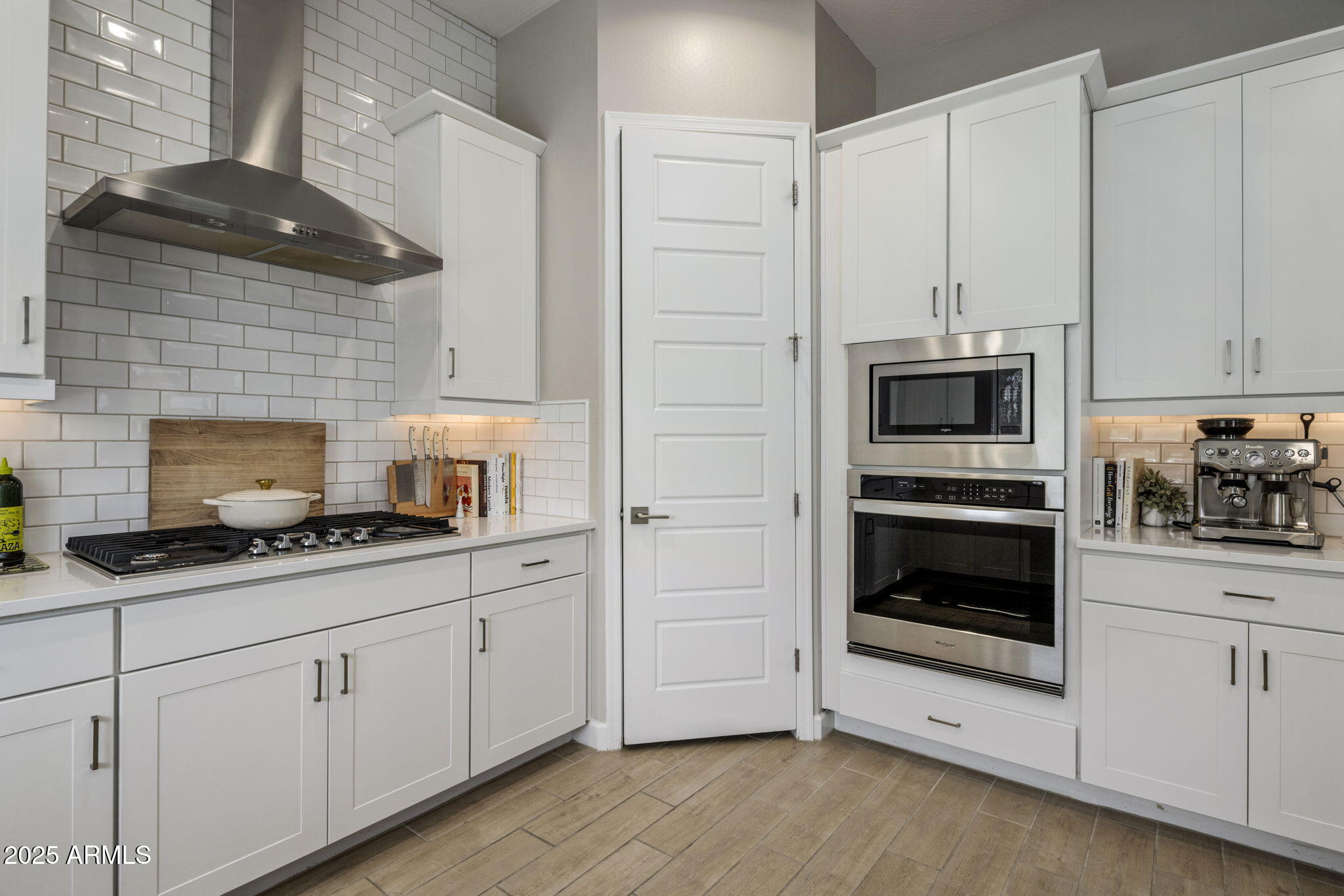 Kitchen with white cabinets, subway tile, gas cooktop, and built-in stainless steel appliances.