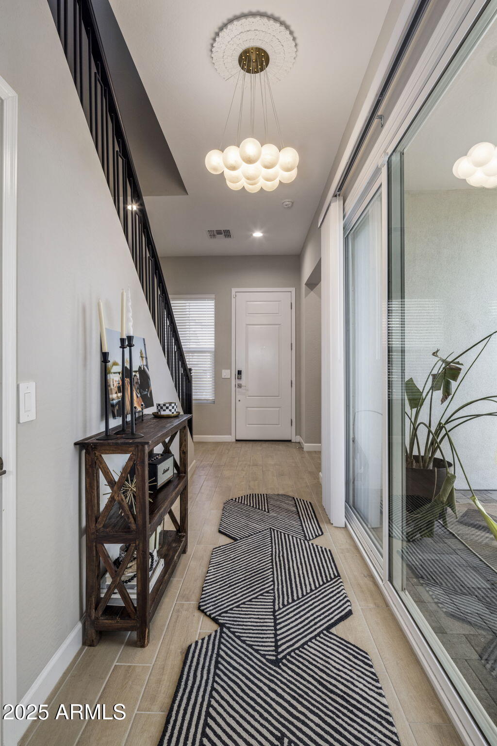 Entry hall with a black-railed staircase, globe chandelier, and geometric striped runners beside sliding glass doors.