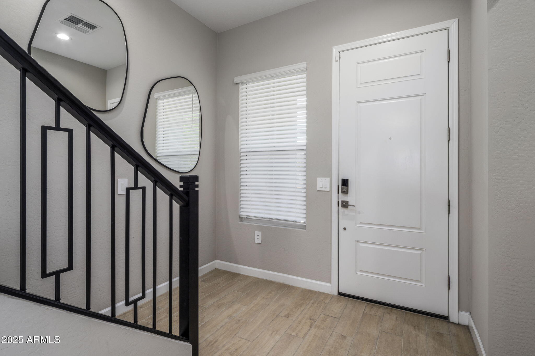 Entry foyer with a white front door, wood-look tile, and black metal staircase railing.