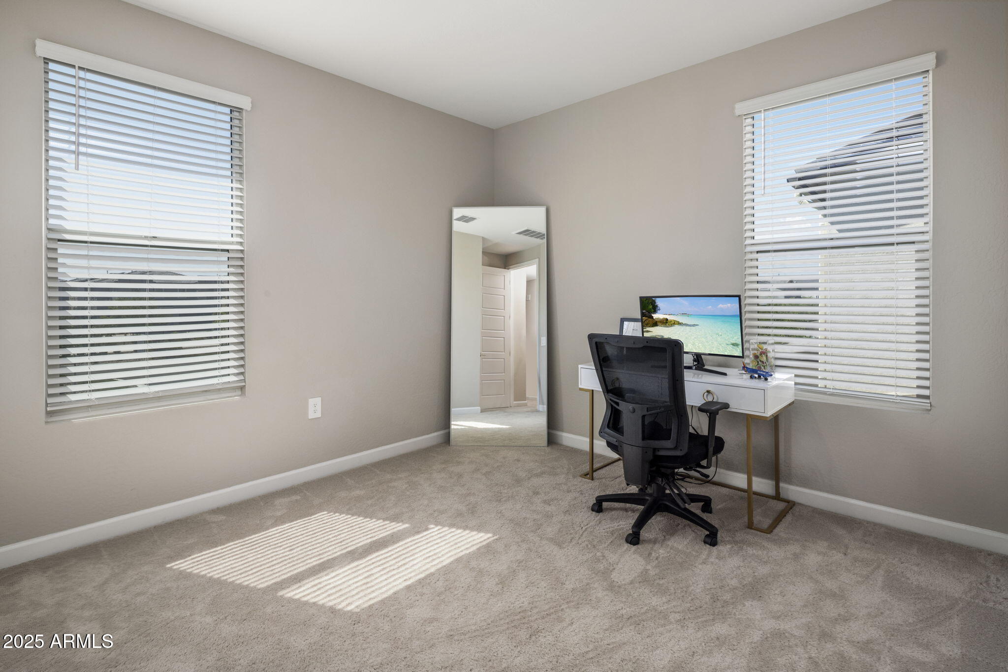Home office with a white desk, black chair, and sunlight across the carpet.