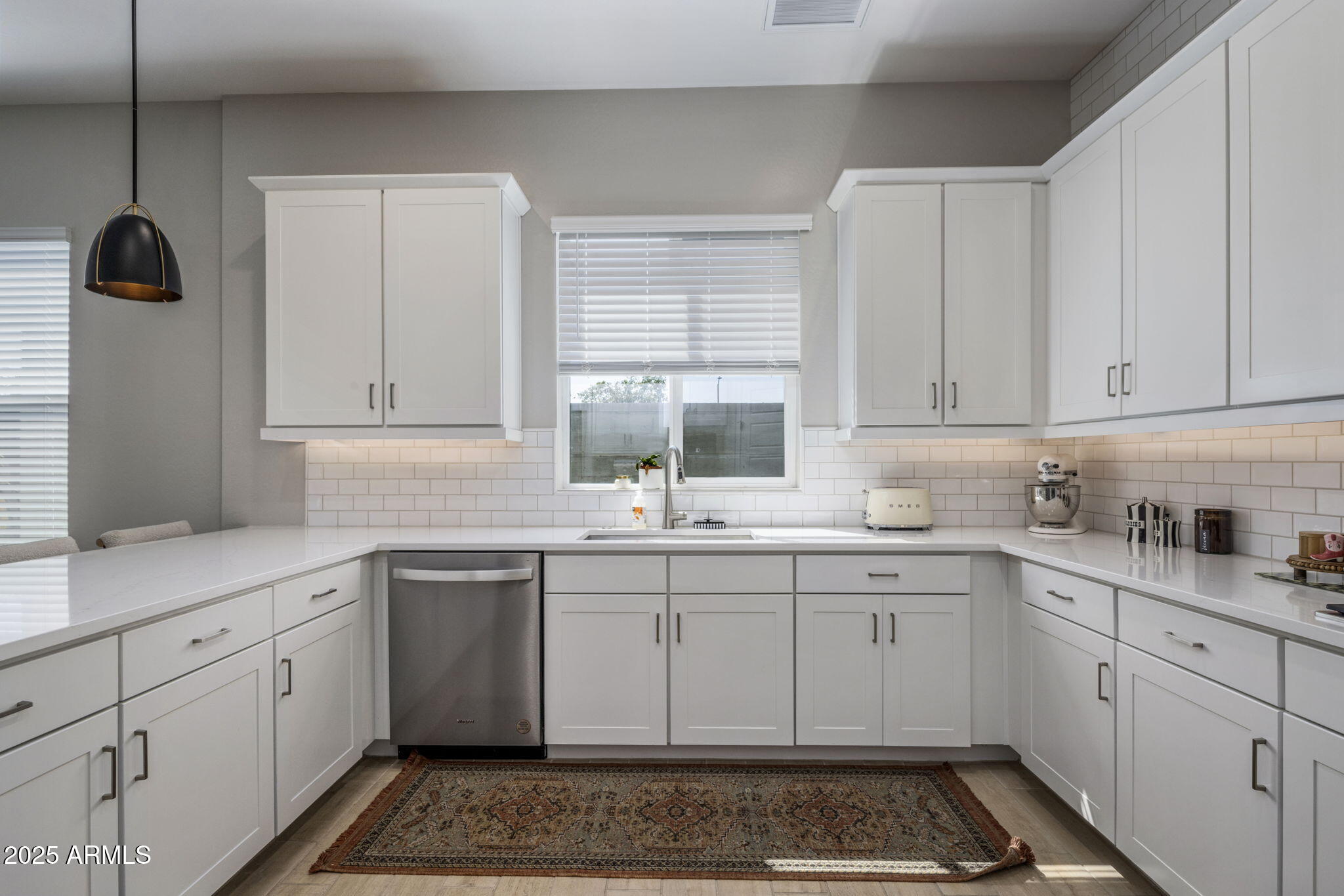 U-shaped kitchen with white cabinets, subway-tile backsplash, stainless steel dishwasher, and patterned rug.
